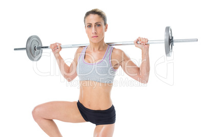 Strong female crossfitter lifting barbell behind head looking at