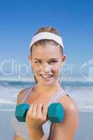 Sporty happy blonde lifting dumbbell on the beach