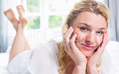 Pretty blonde lying on bed smiling at camera