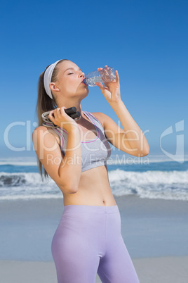 Sporty blonde standing on the beach drinking water