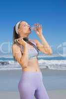 Sporty blonde standing on the beach drinking water