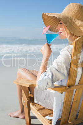 Smiling blonde relaxing in deck chair by the sea sipping cocktai