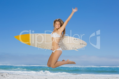 Smiling surfer girl holding her surfboard and jumping on the bea