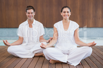 Attractive couple in white sitting in lotus pose smiling at came