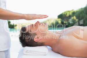 Peaceful man getting reiki treatment poolside