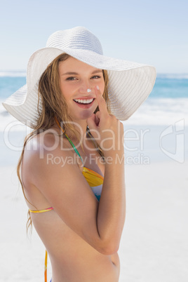 Beautiful girl putting spf on nose on the beach smiling at camer