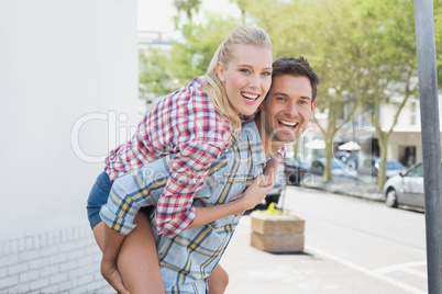 Young hip man giving his blonde girlfriend a piggy back