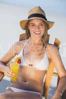 Pretty smiling blonde relaxing in deck chair on the beach with c
