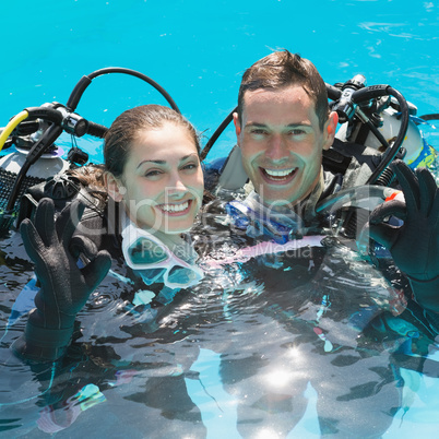 Smiling couple on scuba training in swimming pool showing ok ges