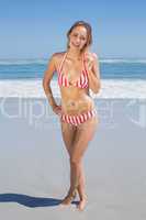 Blonde fit woman in striped bikini at beach smiling at camera