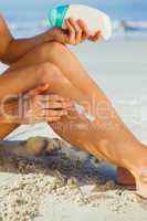 Woman sitting on the beach applying suncream
