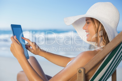 Smiling woman relaxing in deck chair on the beach using tablet