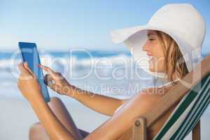 Smiling woman relaxing in deck chair on the beach using tablet