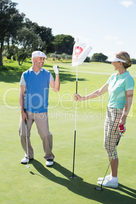 Lady golfer holding eighteenth hole flag for cheering partner