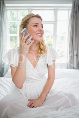 Pretty blonde sitting on bed talking on the phone