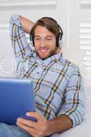 Casual smiling man lying on couch listening to music on tablet p