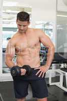 Shirtless focused bodybuilder lifting heavy black dumbbell
