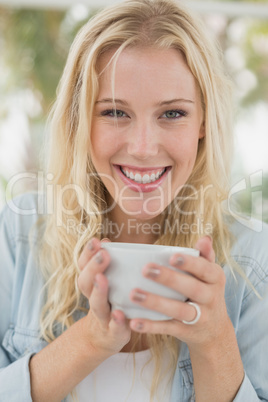 Pretty blonde sitting at table having coffee smiling at camera