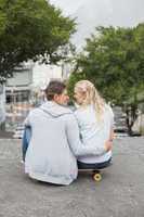 Hip young couple sitting on skateboard smiling at each other