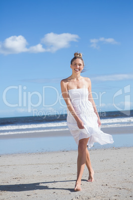 Blonde in white dress walking on the beach smiling at camera