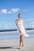 Blonde in white dress walking on the beach smiling at camera