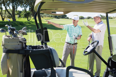 Golfing friends standing beside their buggy looking around