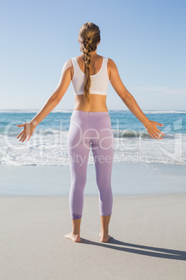 Sporty blonde standing on the beach with arms out