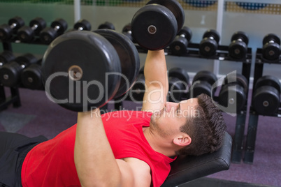 Bodybuilder lying on bench lifting dumbbells