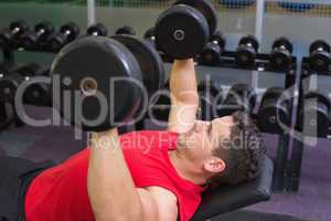 Bodybuilder lying on bench lifting dumbbells