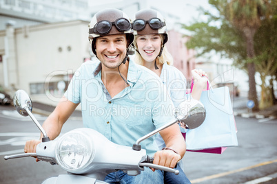 Hip young couple riding scooter with shopping bags