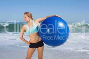 Fit woman standing on the beach holding exercise ball