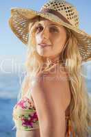 Gorgeous blonde in straw hat and bikini smiling at camera on bea