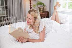 Pretty blonde lying on bed reading a book