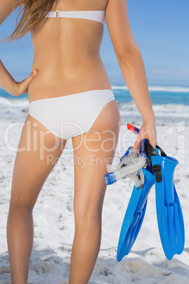 Rear view of fit woman holding fins and snorkel on the beach