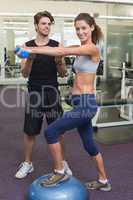 Fit woman stepping on bosu ball holding dumbbell with trainer
