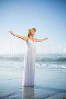 Smiling blonde standing on the beach in white sundress and sunha