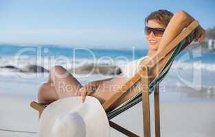 Pretty smiling woman relaxing in deck chair on the beach