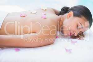 Smiling brunette lying on towel with rose petals