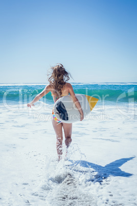 Fit surfer girl running to the sea with her surfboard
