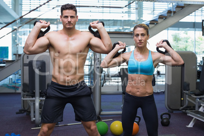 Bodybuilding man and woman lifting kettlebells looking at camera