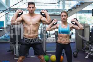 Bodybuilding man and woman lifting kettlebells looking at camera