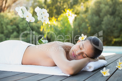 Smiling brunette lying on a towel poolside surrounded by flowers