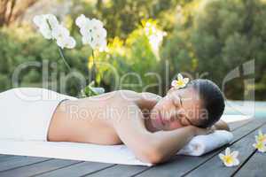 Smiling brunette lying on a towel poolside surrounded by flowers