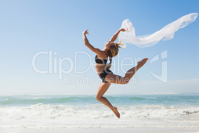 Fit blonde jumping gracefully with scarf on the beach