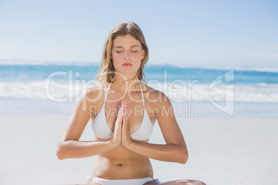 Beautiful girl in white bikini sitting in lotus pose on beach