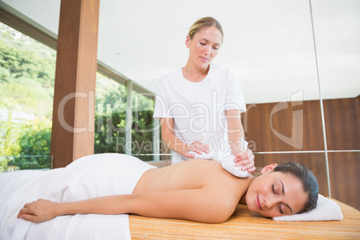 Smiling woman getting a back massage with herbal compresses