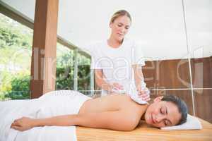 Smiling woman getting a back massage with herbal compresses