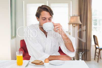 Handsome man having breakfast in his bathrobe drinking coffee