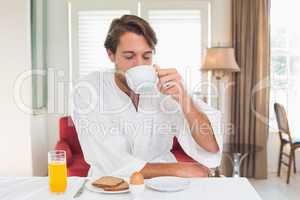 Handsome man having breakfast in his bathrobe drinking coffee