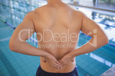 Fit swimmer touching his back by the pool